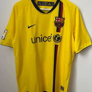 FC Barcelona Messi bortatröja gul Nike M - Gul FC Barcelona bortatröja med Messi 10 på ryggen. Klassisk Nike-design med svart krage, klubbmärke på bröstet och Unicef-tryck. Röd och mörkblå rand på framsidan, LFP-märke på ärmen. Tillverkad i lätt och ventilerande material.