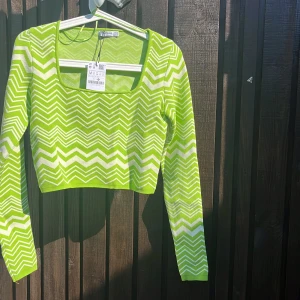 Grönvit zigzag stickad tröja Stradivarius - Säljer en grön och vit stickad tröja från Stradivarius med coolt zigzag-mönster. Tröjan är croppad, har lång ärm och fyrkantig ringning. Perfekt för dig som vill sticka ut med färg och mönster i din outfit.