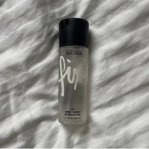 MAC Prep + Prime Fix+ Face Mist - MAC Prep + Prime Fix+ är en genomskinlig face mist i en smidig plastflaska med svart spraykork. Perfekt för att fräscha upp huden eller fixera sminket. Innehåller 100 ml och har en stilren design med vit text på flaskan.