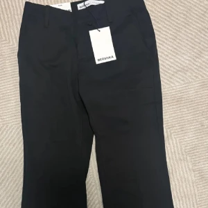Kostymbyxor Bershka - Stilrena svarta kostymbyxor från Bershka med raka, vida ben och pressveck. Byxorna har hällor för bälte och klassisk stängning fram. Helt nya med prislapp. Storlek 34/XS
