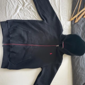 Ralph lauren Tröja - Svart hoodiejacka från Polo Ralph Lauren med dragkedja och huva. Jackan har två stora fickor framtill och en röd logga broderad på bröstet. Tillverkad i mjuk bomull och har en snygg detalj med röd och vit rand på insidan av huvan. Pris kan diskuteras 
