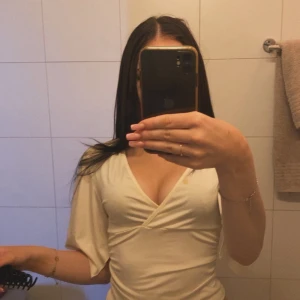 Krämvit omlottopp med v-ringning - Säljer en krämvit omlottopp med djup v-ringning och korta, lösa ärmar. Toppen har en smickrande omlottdesign som framhäver midjan och ger en trendig look. Perfekt att styla med jeans eller kjol för en snygg outfit.