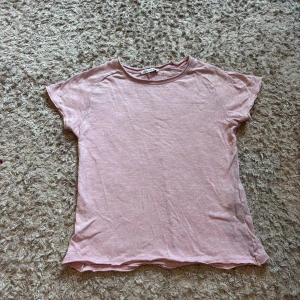 Ljusrosa t-shirt från Zara - Enkel och snygg ljusrosa t-shirt från Zara i mjuk bomull. Modellen är klassisk med rund hals och korta ärmar.T-shirten har en söm längs ryggen som ger en extra detalj.