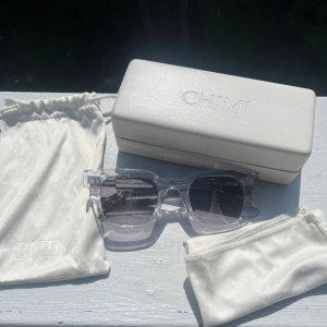 CHIMI 04 CORE - Snygga solglasögon från CHIMI med transparent, fyrkantig båge och gråtonade linser. Kommer med originalfodral och påse. Perfekt accessoar för att lyfta din stil med en modern och clean look.