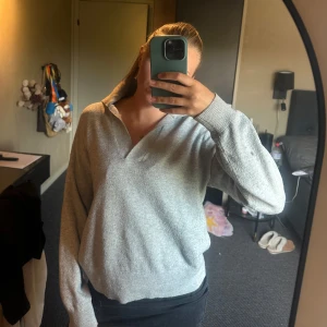 Grå stickad tröja med krage - Mysig grå stickad tröja med avslappnad passform och bred krage. Tröjan har långa ärmar och ribbade muddar vid ärmslut och nederkant. 