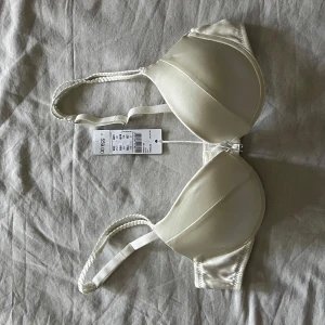 Vit satin bh från intimissimi  - Snygg vit bandeau från Bellissima i satinliknande material. Design med släta kupor och diskreta sömmar utan push up. Perfekt för att bära under toppar eller klänningar där du vill ha en clean look. Justerbara band för bästa passform.