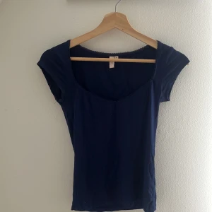 Mörkblå topp med spets från Nelly - Snygg mörkblå topp från Nelly i storlek XS. Toppen har korta ärmar, v-ringad halsringning och en söt spetskant runt halsen. Perfekt att styla med jeans eller kjol för en enkel men chic look.
