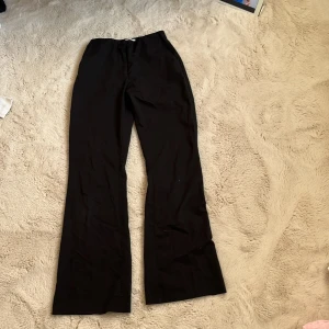 Svarta kostymbyxor från H&M, strl 36 - Svarta kostymbyxor från H&M i klassisk modell med bootcut ben och diskreta bakfickor. Byxorna har dragkedja och knapp framtill samt en stilren look som passar till många olika outfits. Materialet är mjukt och har en lätt stretch.