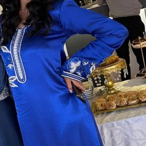 Blå långklänning  - Snygg blå långklänning med v-ringning och långa ärmar. Klänningen har vackra silvriga blombroderier. Köpt från  dubai och endast använd en gång på en fest. Passar bra för 34-36 