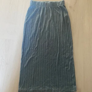 Grå ribbad långkjol från Soyaconcept - Säljer en grå långkjol från Soyaconcept med ribbad struktur och elastisk midja. Kjolen är mjuk och stretchig, perfekt för en chill och stilren look. Materialet är en mix av viskos och polyester med lite elastan för extra komfort.