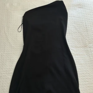 Svart ribbad one shoulder klänning - Säljer en svart ribbad klänning med one shoulder-design och tunna axelband. Klänningen är figurnära och har en kort längd, perfekt för dig som gillar en stilren och trendig look.