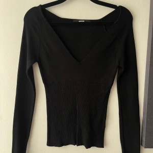 Svart ribbad v-ringad tröja Bik Bok - Snygg svart långärmad tröja från Bik Bok med djup v-ringning och ribbad midja. Tröjan är figurnära och har en stilren look som passar perfekt till jeans eller kjol. Materialet är stretchigt och mjukt.