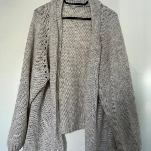 Grå stickad kofta, HeartKiss, S/M - En ljusgrå stickad kofta med en öppen front och långa ärmar från märket HeartKiss. Storlek S/M. Koftan har en avslappnad passform och en mjuk textur. 57% polyacryl, 29% polyamide, 7% viskos och 7% ull. Mycket fint skick.  Längd ca 47 cm.