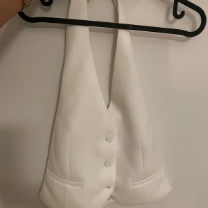 Vit omlottväst från MNG - Snygg vit väst från MNG i omlottmodell med djup v-ringning och två knappar framtill. Västen har två fejkade fickor och är tillverkad i ett slätt tyg som ger en clean look. Perfekt för att lyfta din outfit med en modern touch.