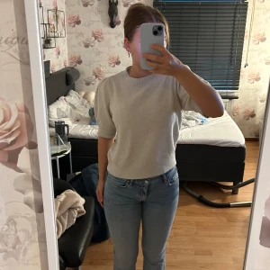 Beige stickad topp med puffärm - Superfin beige stickad topp med korta puffärmar och rund hals. Tröjan har ribbade muddar vid ärmslut och midja, vilket ger en snygg passform. Perfekt att styla med jeans för en clean look.