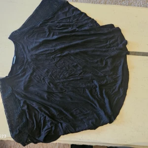 Svart topp med virkade ärmar Vanizza - Svart topp från Vanizza med snygga virkade detaljer längs ärmarna. Modellen är lös och har rund halsringning. Perfekt för dig som gillar en chill och stilren look med en twist. Toppens material känns mjukt och lätt mot huden.