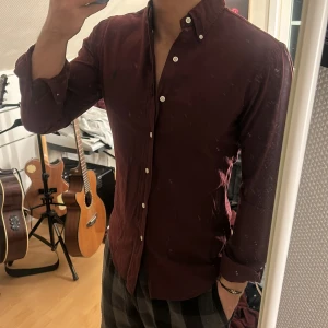 Vinröd skjorta från Ralph Lauren - Snygg vinröd skjorta från Ralph Lauren med klassisk krage och knappar framtill. Skjortan har en broderad logotyp på bröstet och långa ärmar. Perfekt för en stilren look.