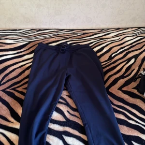 Mörkblå mjukisbyxor med snörning - Säljer ett par mörkblå mjukisbyxor med elastisk midja och snörning. Byxorna har raka ben och är tillverkade i mjukt material som är skönt att ha på sig. Perfekta för chill dagar eller när du vill vara bekväm. Den här tecken på användning men inga skador elle hål 