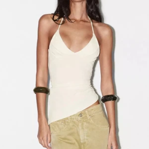 Havsgrön halterneck topp - Snygg havsgrön tubtopp med halterneck och djup v-ringning. Toppen har en asymmetrisk nederkant och är figurnära med smala band runt nacken. Perfekt för dig som gillar minimalistisk och trendig stil.