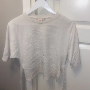 Trendig topp med knyt i rygg från Nelly - Säljer en trendig vit topp från Nelly i storlek XS som ofta är slutsåld. Inga defekter och säljer pga den är för liten. Använd sällan och enstaka gånger. 