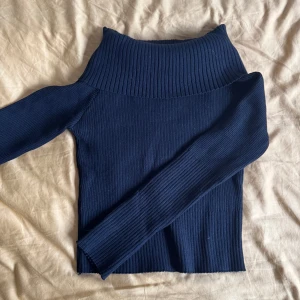 Svart  ribbad polotröja - Snygg mörkblå ribbad polotröja med hög krage och lång ärm. Tröjan är figurnära och har en stilren look med bred ribbstickning vid hals, ärmslut och nederkant. Perfekt för dig som gillar en enkel men trendig stil.