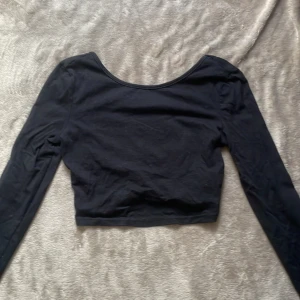 Svart rygglös croppad topp från SHEIN - Svart långärmad croppad topp från SHEIN med rundad, djup urringning både fram och bak. Tillverkad i mjuk bomullsmix som känns skön mot huden. Perfekt att styla med höga jeans eller kjol för en clean look.