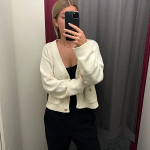 Vit ribbad kofta med knappar - Säljer en stilren vit kofta med ribbad struktur och knappar framtill. Koftan har en v-ringad design och långa ärmar, perfekt för lager-på-lager under kyligare dagar.