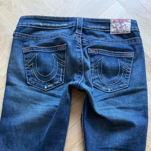 Blå jeans från True Religion - Snygga blå jeans från True Religion med klassiskt broderade bakfickor samt brodering på en av fickorna fram. De har en låg midja och en bootcut-stil. Bra skick i storlek 27. Pris kan diskuteras. 