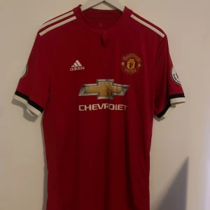 Röd Manchester United fotbollströja authentic - Säljer en röd Manchester United fotbollströja från Adidas med Chevrolet-logga på framsidan. Tröjan har korta ärmar och vita detaljer på axlarna. Perfekt för fans av laget! Nr3 Bailly storlek L