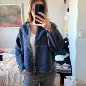 Blå cardigan jacka med knappar - Säljer en snygg blå cardigan jacka med knappar och vita sömmar. Jackan har en normal passform och långa ärmar. Perfekt för en stilren look.