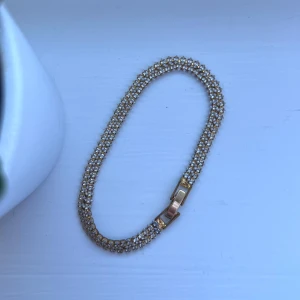 Guldigt med strass - Elegant guldarmband prytt med glittriga stenar. Perfekt för att ge en touch av glamour till din outfit. Armbandet har en säker låsning och en klassisk design som passar till många tillfällen. Har blivit lite mörkt på insidan - se sista bilden! Önskar du veta exakta mått? Tveka inte att höra av dig!