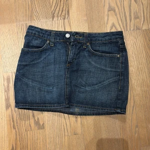 Jeanskjol från Lucky Rose - Snygg jeanskjol från Lucky Rose i mörk denim med klassisk femficksdesign. Kjolen har en knapp och dragkedja framtill samt broderad logga baktill. Perfekt för en avslappnad stil. Säljer den pga den är för liten men knappt använd med nytt skick 