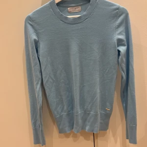 Ljusblå tröja från Holly & Whyte - Säljer en stilren ljusblå tröja från Holly & Whyte by Lindex. Tröjan har långa ärmar och ribbade muddar med dekorativa knappar. Perfekt för en avslappnad men ändå elegant look. 💙