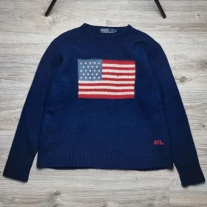 Ralph Lauren tröja - Sällsynt Ralph Lauren tröja i marinblå ull med amerikanska flaggan på bröstet🇺🇸🤩  Storlek: L (sitter som M) Nypris: 5000 kr – extremt svår att få tag på!  Skick: Mycket bra, endast ett litet hål (se bild 2) Mått: – Bröst: 54 cm – Längd: 61 cm  Fraktar alltid samma dag som köp! 😀🤝