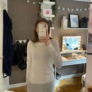 Vit stickad tröja - Säljer en stilren vit stickad tröja med kabelstickat mönster. Tröjan har långa ärmar och en klassisk passform som passar perfekt till kyligare dagar. Perfekt för en avslappnad och mysig look.