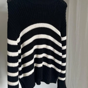 Svart och vit randig stickad tröja från Gina Tricot - Säljer en snygg svart och vit randig stickad tröja från Gina Tricot. Tröjan har en ribbad krage och långa ärmar, perfekt för kyligare dagar. Den är både stilren och bekväm.