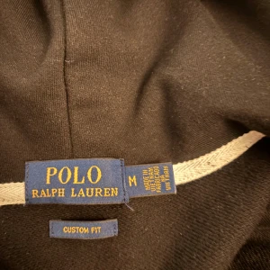 Svart hoodie från Polo Ralph Lauren - Säljer en stilren svart hoodie från Polo Ralph Lauren med dragkedja och huva. Den har en broderad logotyp på bröstet och ribbade muddar vid ärmslut och nederkant. Perfekt för en avslappnad stil. Storleken passar både M och S. det är bara att höra av er!!!! Är även öppen för byten!