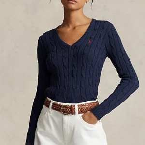 Mörkblå ribbad tröja med v-ringning - Snygg mörkblå tröja från Ralph Lauren med v-ringning och ribbad design. Perfekt för en stilren look. Tröjan har långa ärmar och en liten logga på bröstet.