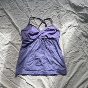 Lila linne med korsade axelband - Säljer ett snyggt lila linne med korsade axelband och v-ringad
