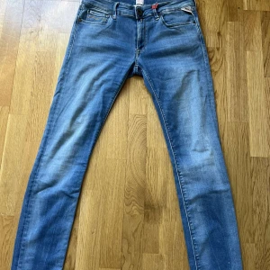 Blå jeans från Replay - Snygga blå jeans från Replay med en klassisk femficksdesign och knappgylf. De har en diskret sliten look och en liten broderad logga på bakfickan.