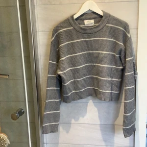 Grå randig tröja från Zara - Säljer en snygg grå tröja från Zara med vita ränder. Tröjan är ribbad och har en croppad design med långa ärmar. Perfekt för en stilren look. Den går till midjan. Använd ett fåtal gånger.