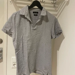 Grå kortärmad pikétröja från Massimo dutti  - Snygg grå pikétröja från Massimo dutti med korta ärmar och klassisk krage. Perfekt för en avslappnad stil. Tröjan har en diskret mönstring som ger den en extra touch.