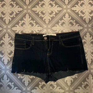 Mörkblåa low waist jeans shorts - Snygga mörk blåa jeansshorts med fransiga kanter och klassisk femficksdesign. Perfekta för en avslappnad stil. De har en knapp och dragkedja framtill.