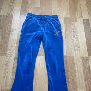 Blå mjukisbyxor från Juicy Couture - Snygga blå mjukisbyxor från Juicy Couture med glittrande JC-logga på ena benet. Byxorna har snörning i midjan och två bakfickor. Säljs för att de inte används🥰