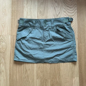 Grön kjol från H&M - Snygg grön kortkjol från H&M med justerbart bälte och knappar framtill. Kjolen har praktiska fickor både fram och bak. Aldrig använd ❤️