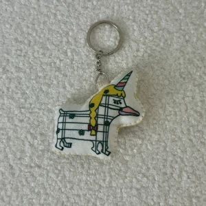 Nyckelring med enhörningsmotiv - Charmig nyckelring med ett unikt enhörningsmotiv. Enhörningen har en gul man och ett randigt mönster med blommor. Perfekt som en söt accessoar till dina nycklar eller väska.