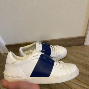 Valentino Open - Snygga Valentino Garavani sneakers i vitt skinn med en bred blå rem över ovansidan. Skorna är använda men nästan i nyskick. Vid snabb affär kan priset diskuteras