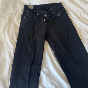 Svarta jeansbyxor från Levi's - Snygga svarta jeansbyxor från Levi's med knappgylf och klassisk femficksdesign. Byxorna har en rak passform och är perfekta för en stilren look. Levi's-logga syns på baksidan. W25 L30