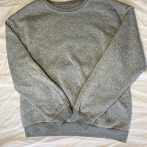 Grå sweatshirt - Säljer en klassisk grå sweatshirt med rund hals och långa ärmar. Perfekt för en avslappnad stil. Tröjan har ribbade muddar vid ärmslut och nederkant.