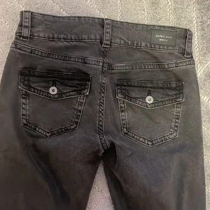 Svarta jeans från Perfect Jeans - Snygga svarta jeans från Perfect Jeans med knappar och fickor bak. De har en klassisk design med en rak passform och är perfekta för en stilren look.